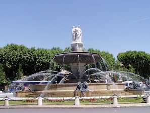 Une grande fontaine dotée de nombreux jets d’eau et de statues à sa base, entourée de verdure et sous un ciel dégagé.