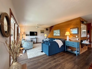 A cozy living room with a blue sofa, a wooden accent wall, a flat-screen TV, and a decorative fish sculpture.