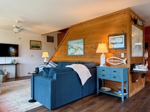 Un salon chaleureux avec un canapé bleu, des murs en bois, un ventilateur de plafond et un téléviseur.