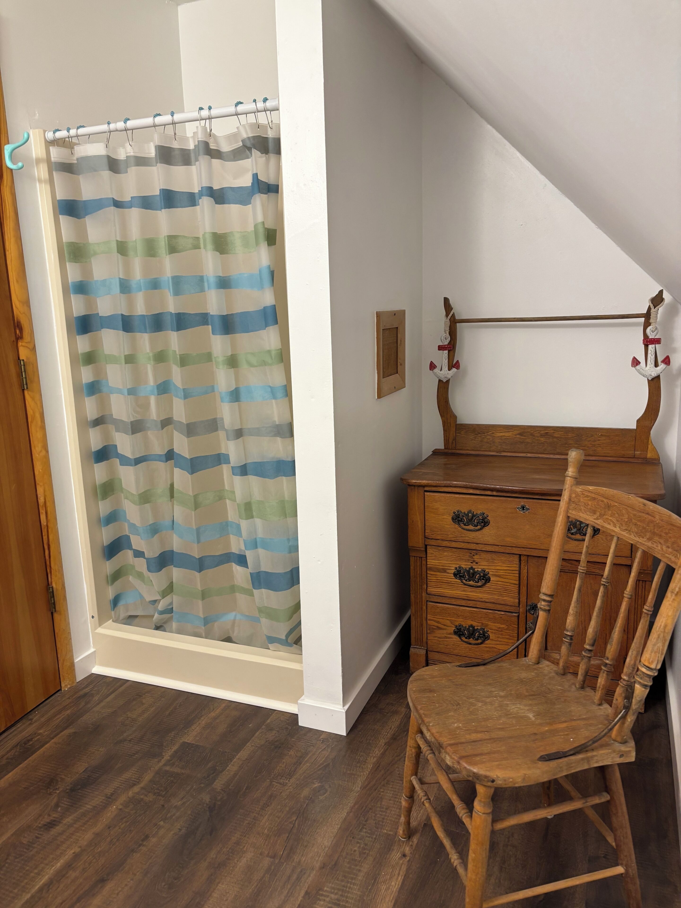 A room with a shower curtain, wooden dresser, and chair.