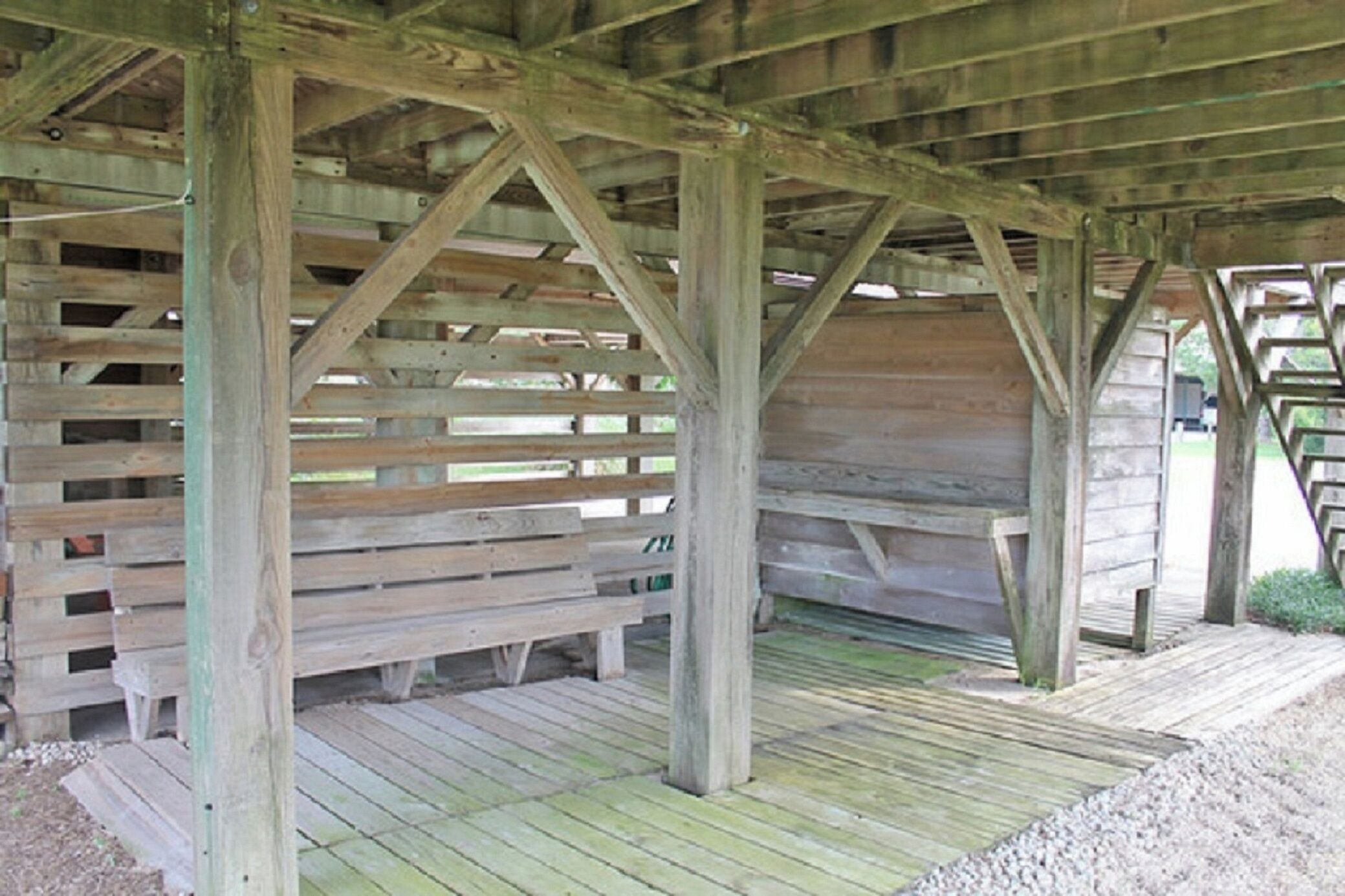 A wooden structure with a slatted roof and wooden benches.