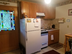 Una cucina con mobili in legno, un frigorifero bianco, un fornello e una finestra con decorazioni in vetro colorato.