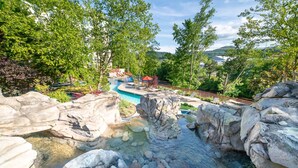 A natural rock pool with clear water, surrounded by large boulders and trees.