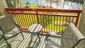 A balcony with two chairs and a small table, overlooking a river and a gazebo.