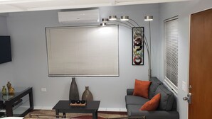 A living room with a flat-screen TV, a sofa with orange cushions, a coffee table with decorative items, and a wall-mounted air conditioner. - Home away from home ... secure and serene location with all the comforts of home (Christiansted)