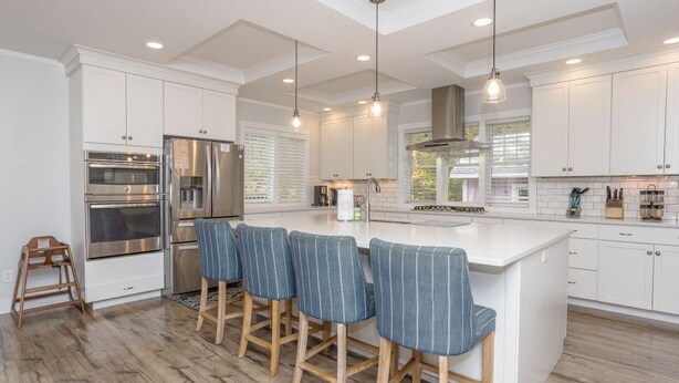 A modern kitchen with white cabinetry, stainless steel appliances, and a central island with bar stools.