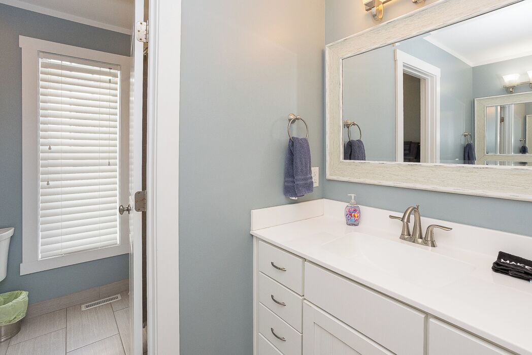 A bathroom with a white vanity, a large mirror, and a window with blinds.