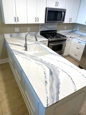 A kitchen with white cabinets, a stainless steel microwave, a stove, and a marble countertop. - Waterscape A526 - Great for Families! (Fort Walton Beach)