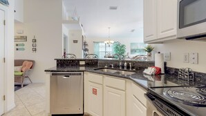 Cocina moderna equipada con lavavajillas, estufa y microondas. Hay una zona de comedor con una silla y un sofá.