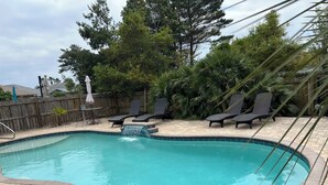 Una piscina con una cascada, rodeada de sillones de descanso y una valla de madera.