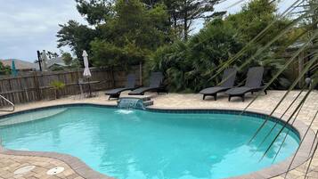 A swimming pool with a waterfall feature, surrounded by lounge chairs and a wooden fence.