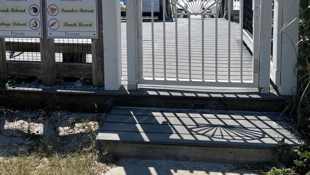 Una entrada cerrada con un letrero de 'NO ENTREN' y un camino de madera, además de indicaciones hacia refugios privados en la playa.