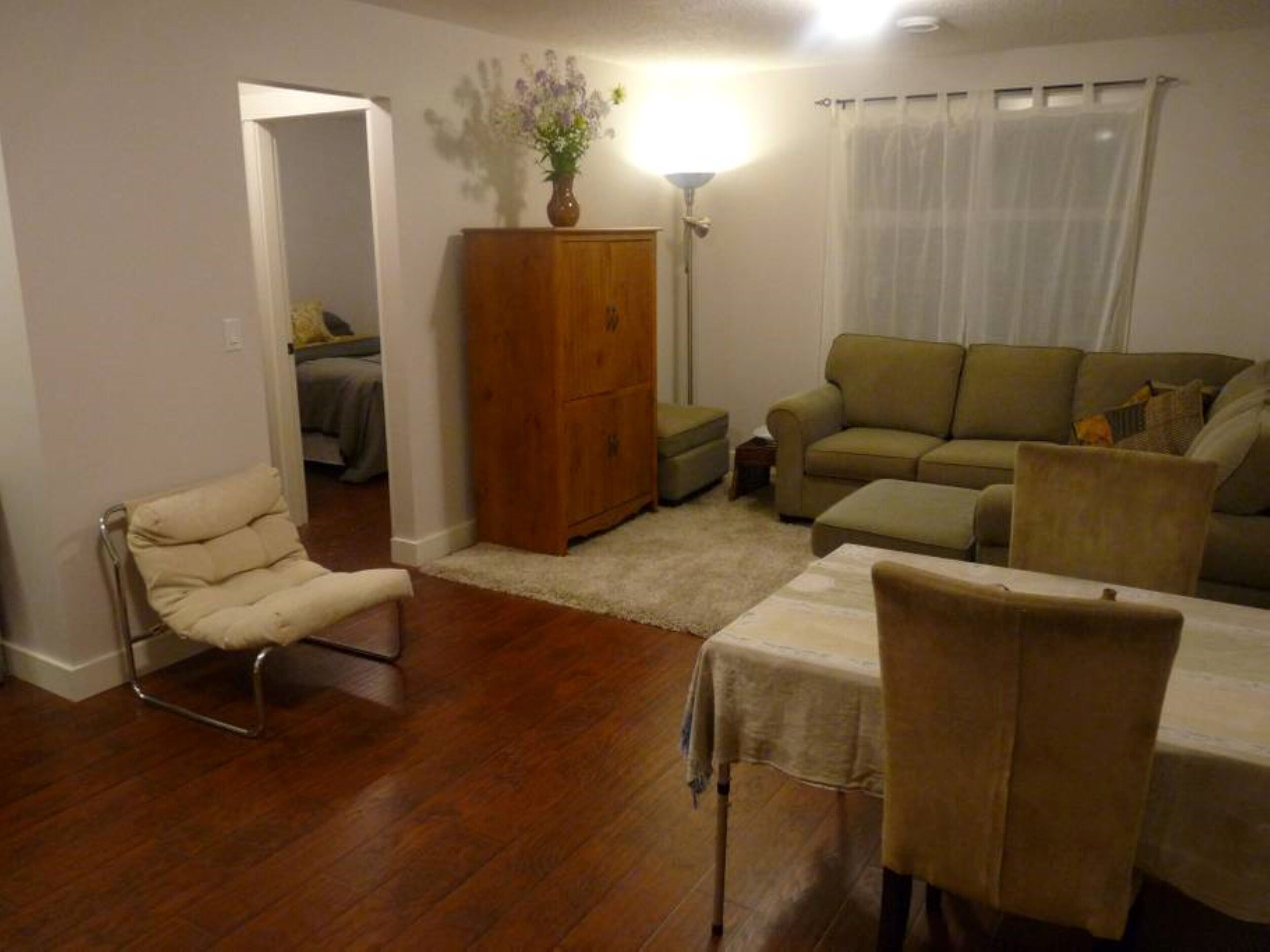 Un salon avec un plancher en bois, un canapé, un fauteuil, une table et un meuble.