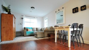 A living room with a wooden floor, a sofa, a dining table with chairs, and a mirror on the wall. - Potters View Guesthouse, Parksville (Parksville)