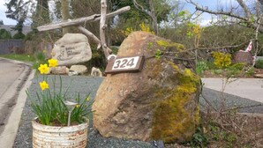 A rustic stone sign with the number 324, a wooden cross, and a rustic pot with daffodils. - Potters View Guesthouse, Parksville (Parksville)