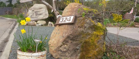 A rustic stone sign with the number 324, a wooden cross, and a rustic pot with daffodils.