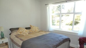 A bedroom with a bed, a nightstand, a window with curtains, and a view of greenery outside. - Potters View Guesthouse, Parksville (Parksville)