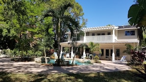 A two-story house with a pool, surrounded by lush greenery and palm trees.