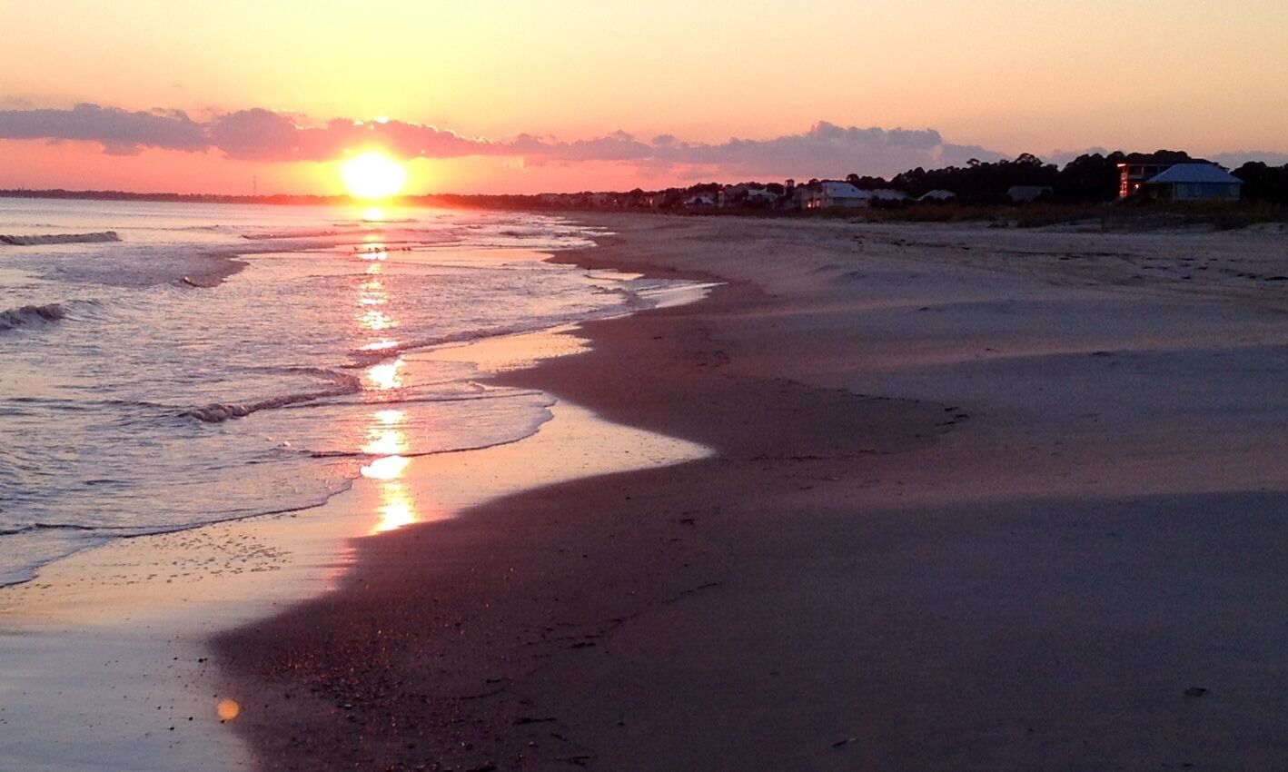 Une plage au coucher du soleil, avec le soleil qui se reflète sur l’eau.
