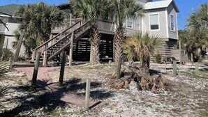 A two-story house with a balcony, a wooden staircase, and palm trees in the yard. -  The Beach House on Florida's Forgotten Coast (St. Joe)