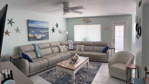 A living room with a beige sofa, a coffee table, a TV, and a ceiling fan. - ~ Music by the Sea ~ On the Beach ~ Hear the Ocean Surf~ (Indian Rocks Beach)