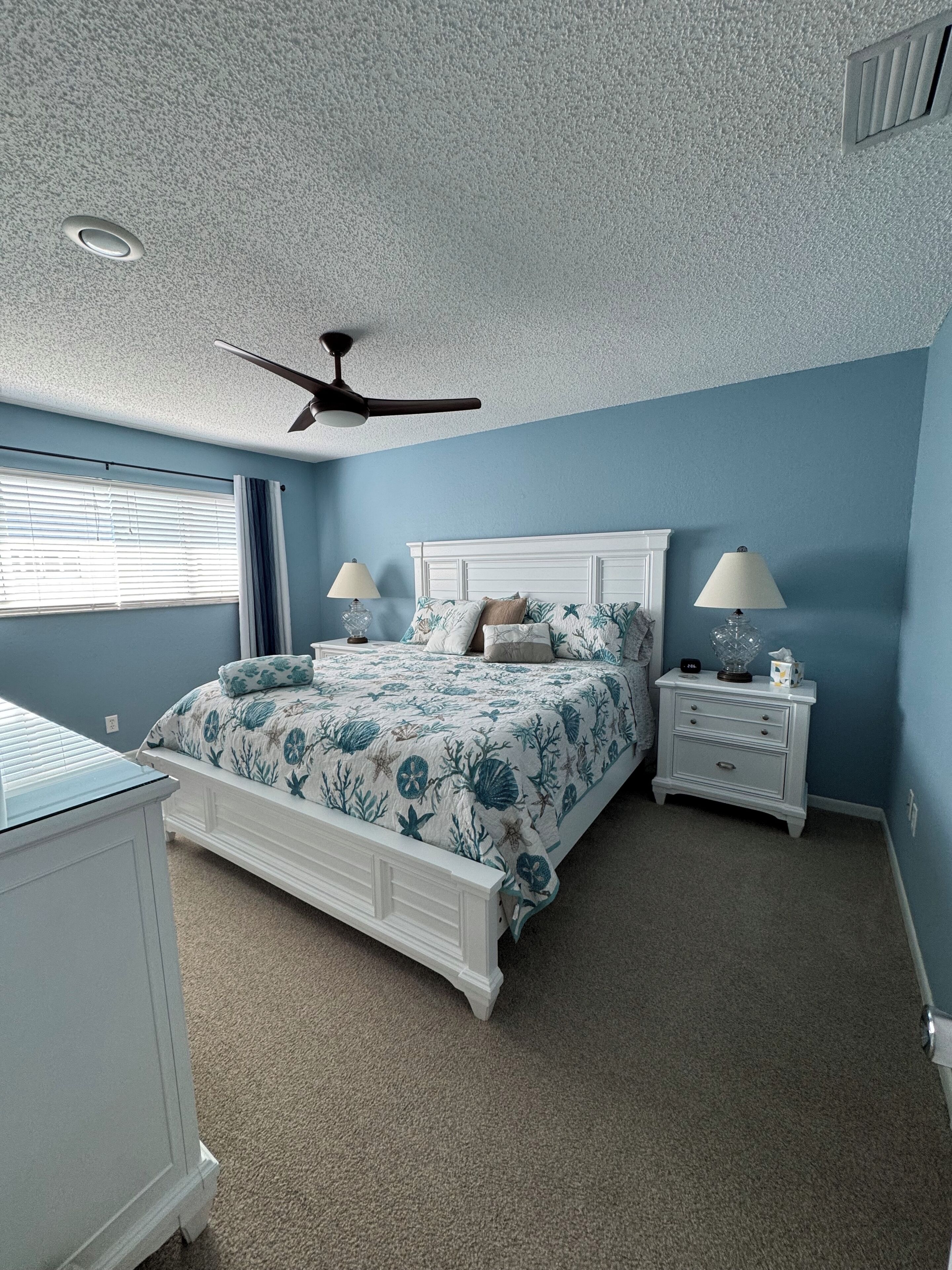 A bedroom with a bed, two bedside tables, a ceiling fan, and a window with blinds.
