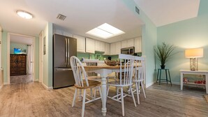 A modern kitchen with white cabinetry, a stainless steel refrigerator, and a dining area with white chairs and a wooden table.