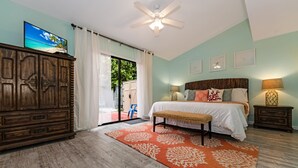 A bedroom with a bed, a ceiling fan, a wooden dresser, and a view through a sliding glass door.