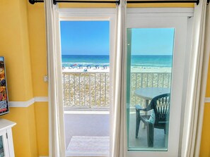 Una habitación con vista a la playa, un balcón con mesa y sillas, y una puerta que da a la playa.