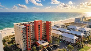 Un hotel frente a la playa con varias construcciones, un estacionamiento y vista al océano.
