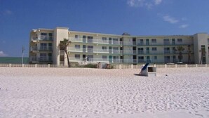 Un hotel frente a la playa con varios pisos, balcones y una playa arenosa.