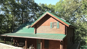 A log cabin with a green roof, a porch with chairs, and a view of a lake.