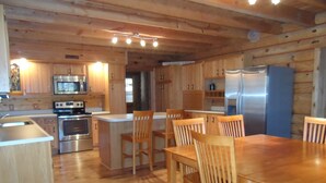 A wooden interior with a kitchen area including a refrigerator, microwave, stove, and wooden chairs around a table.