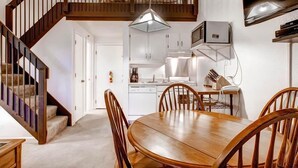Ein Essbereich mit Holztisch und -stühlen, eine Küche mit weißen Schränken und eine Treppe mit Holzhandläufen.