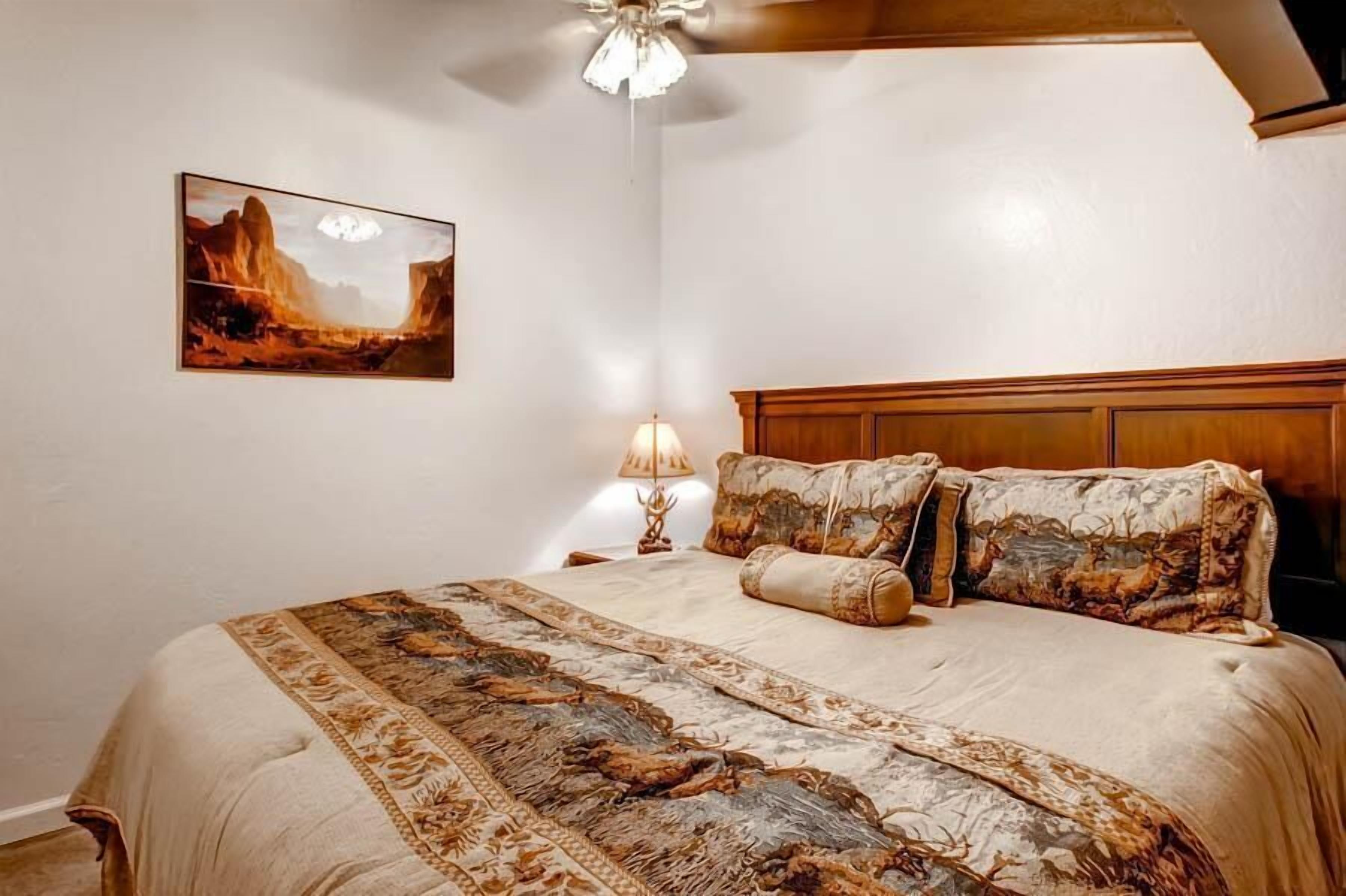A bedroom with a large bed, a headboard, a nightstand, a lamp, and a painting on the wall.