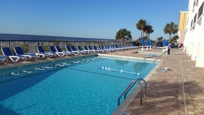Una piscina con agua cristalina azul, rodeada de sillas reclinables azules y palmeras.
