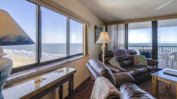 Una habitación con un amplio ventanal con vistas al océano, un sofá de cuero, una mesita y una lámpara.