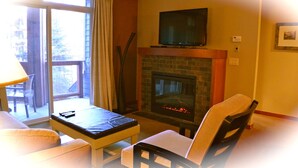 A living room with a fireplace, a television mounted above it, and a sofa. - Enjoy Mountain Views @ Fully Equipped 2BR2BA Hotel Condo (Canmore)
