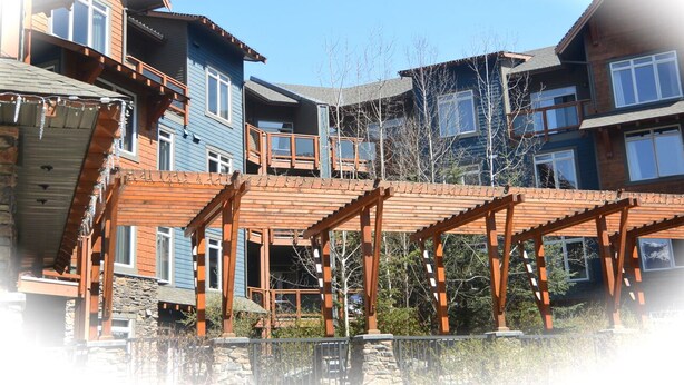 A multi-story building with a wooden deck and stone foundation. - Enjoy Mountain Views @ Fully Equipped 2BR2BA Hotel Condo (Canmore)