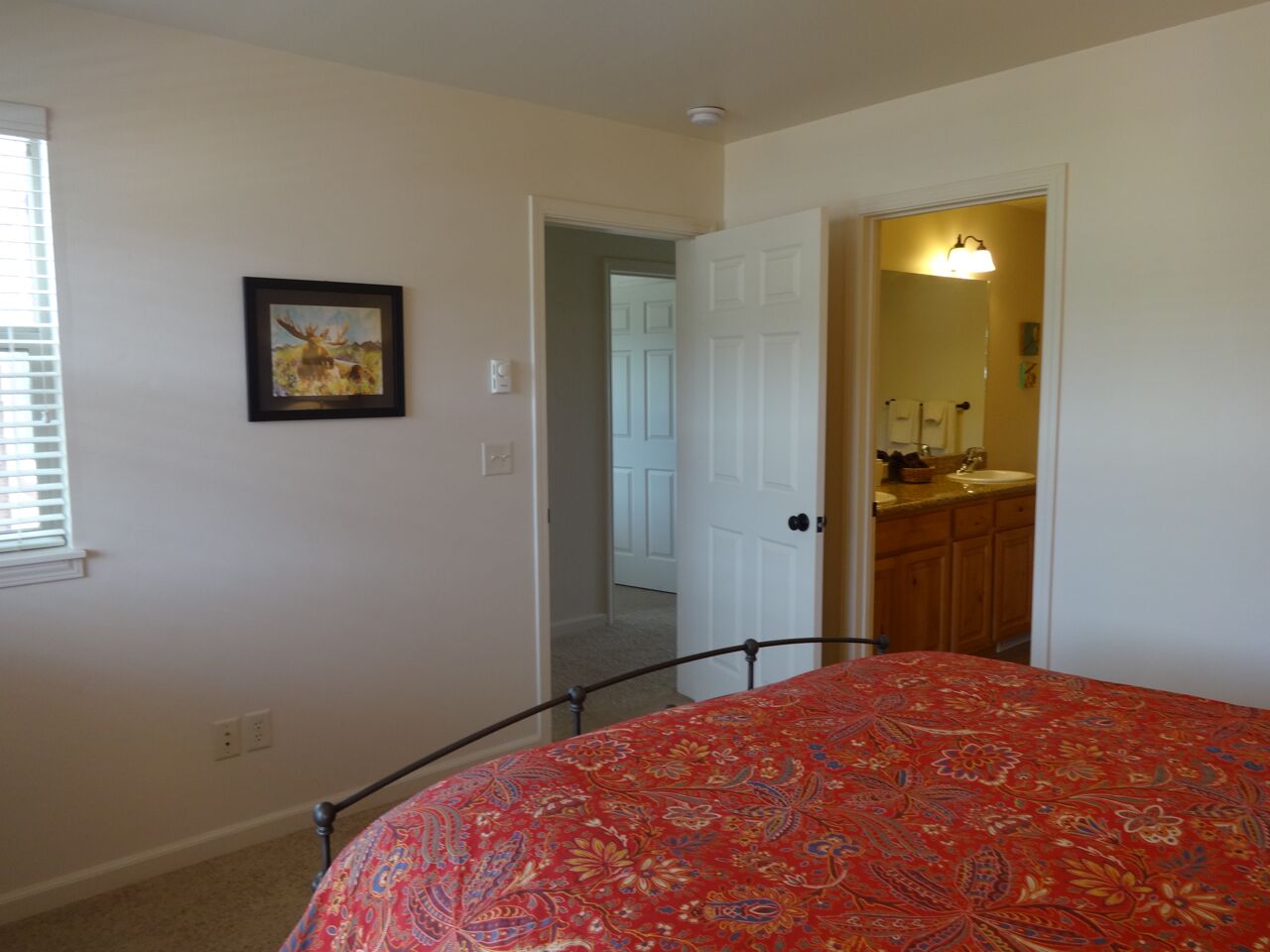 Une chambre à coucher avec un lit, une porte donnant sur une salle de bain et un tableau encadré au mur.