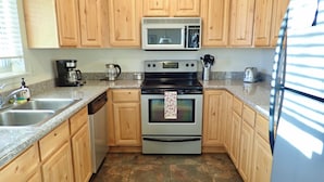 A kitchen with wooden cabinets, a stainless steel sink, a microwave, a stove, and a refrigerator.