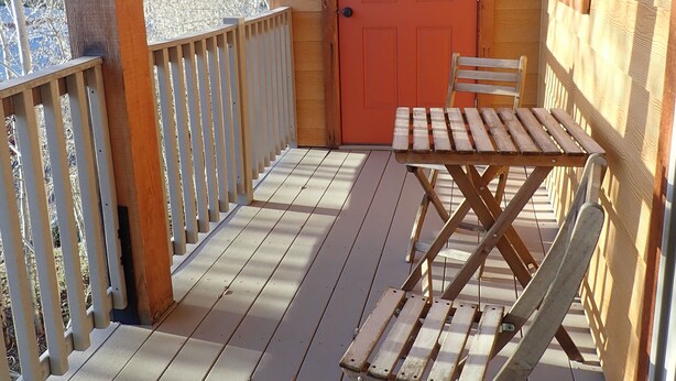 A wooden deck with a table and chairs, a red door, and a view of trees.
