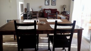 A dining area with a wooden table and chairs, a hanging light fixture, and a sofa in the background.