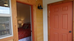 A bedroom with a bed, a nightstand, a lamp, and a wooden door.