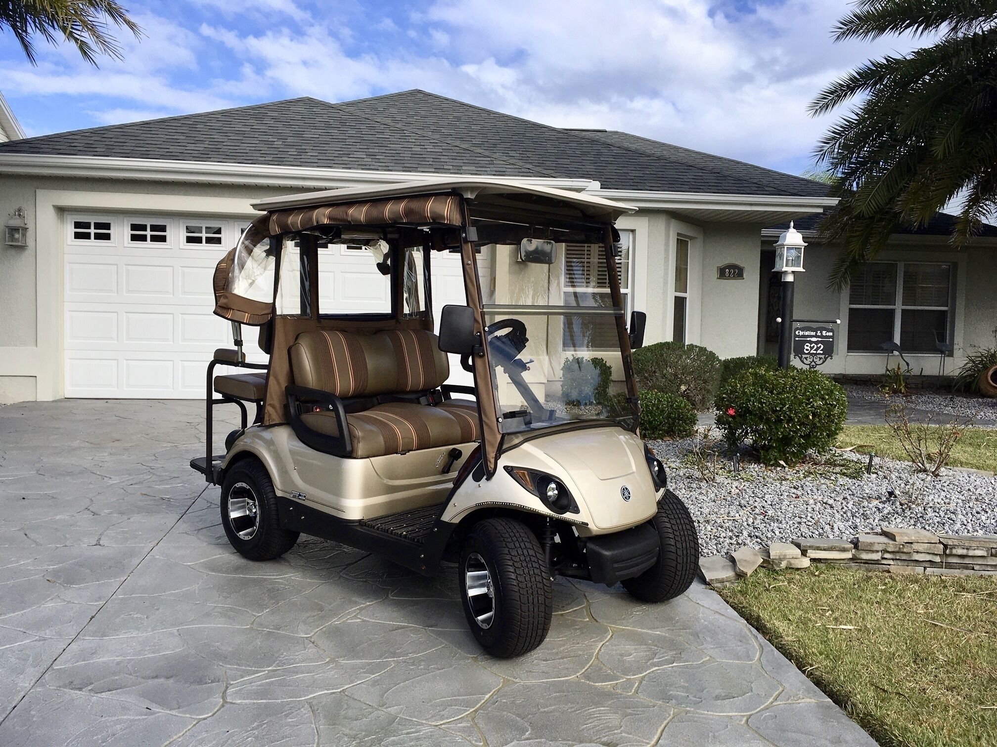 Une voiturette de golf est garée devant une maison qui a un garage, un petit jardin et un lampadaire.