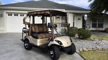 A golf cart parked in front of a house with a garage, a small garden, and a street lamp.