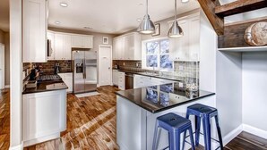 Una cocina moderna con armarios blancos, una isla central con taburetes y suelo de madera.