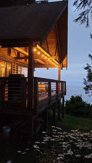 Una baita di legno con un balcone vista acqua, luci a stringa e un'area erbosa con margherite.