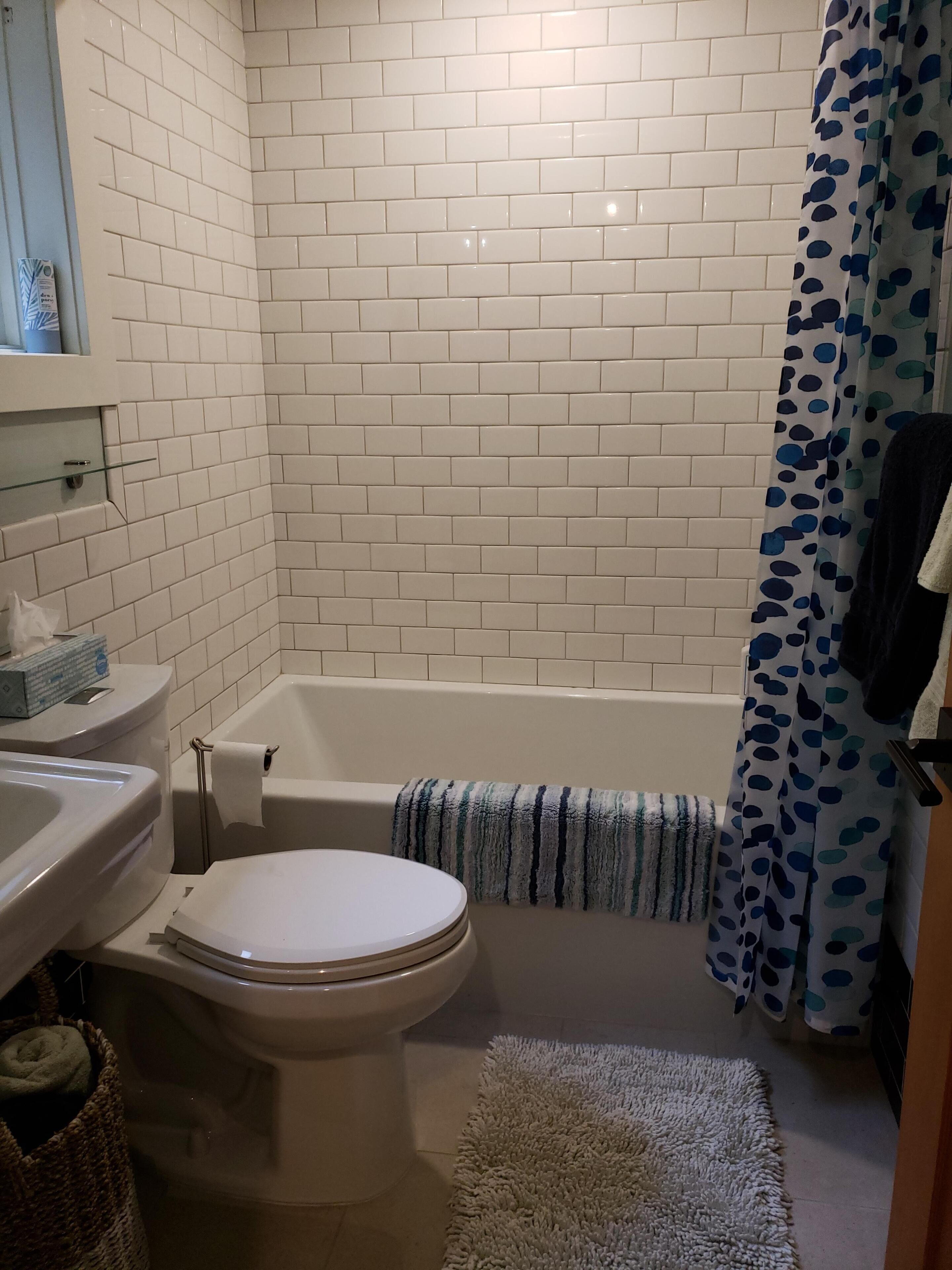 A bathroom with white tiled walls, a white toilet, a bathtub, and a shower curtain with blue polka dots.
