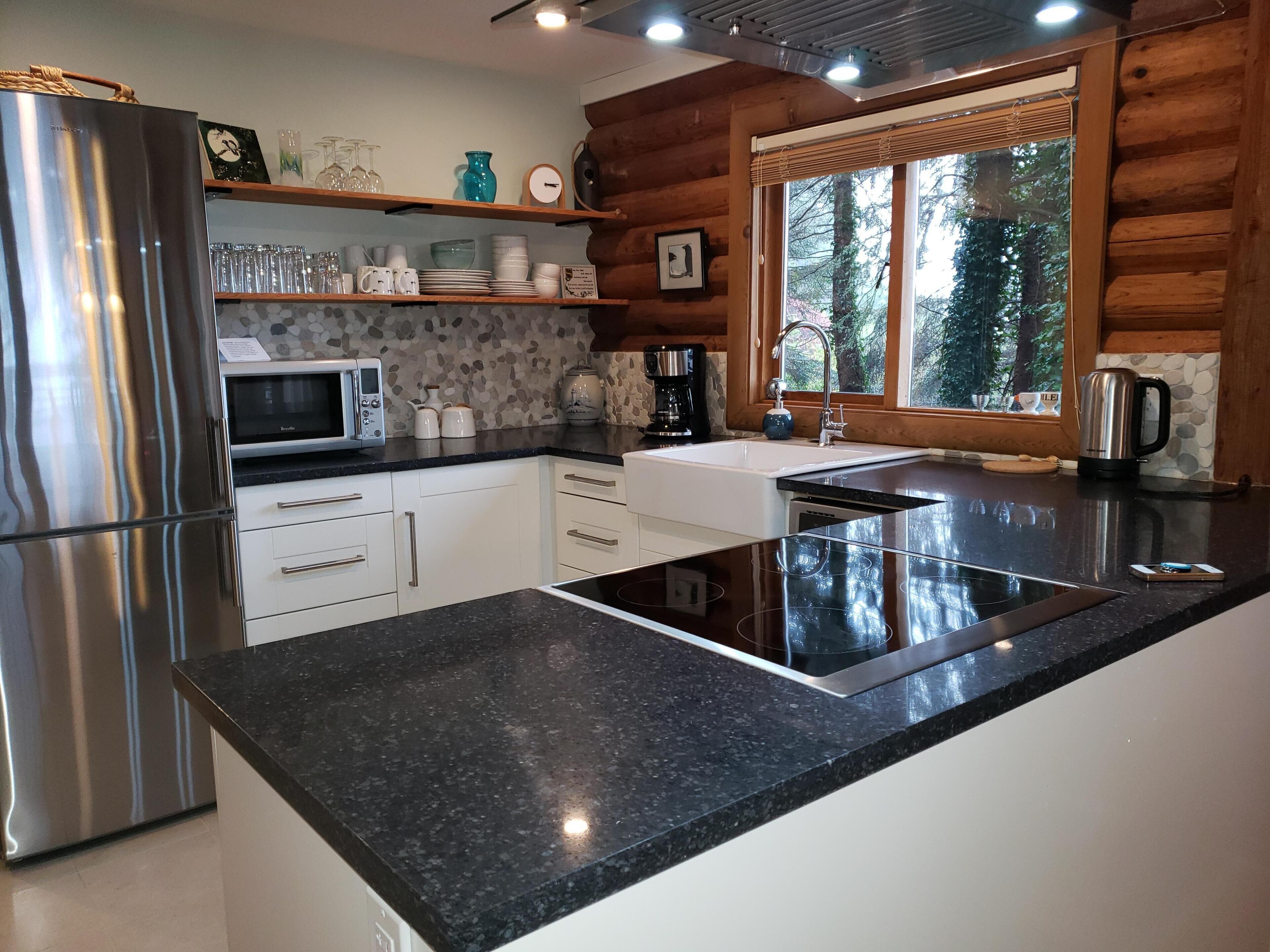 A modern kitchen with a stainless steel refrigerator, a microwave, a sink, and a window with a view of trees.